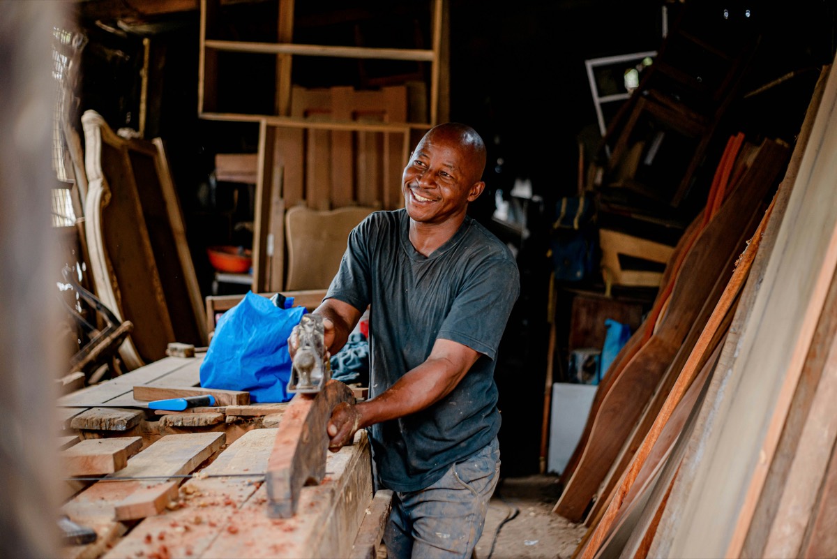Un artisan menuisier souriant rabote une pièce de bois dans son atelier